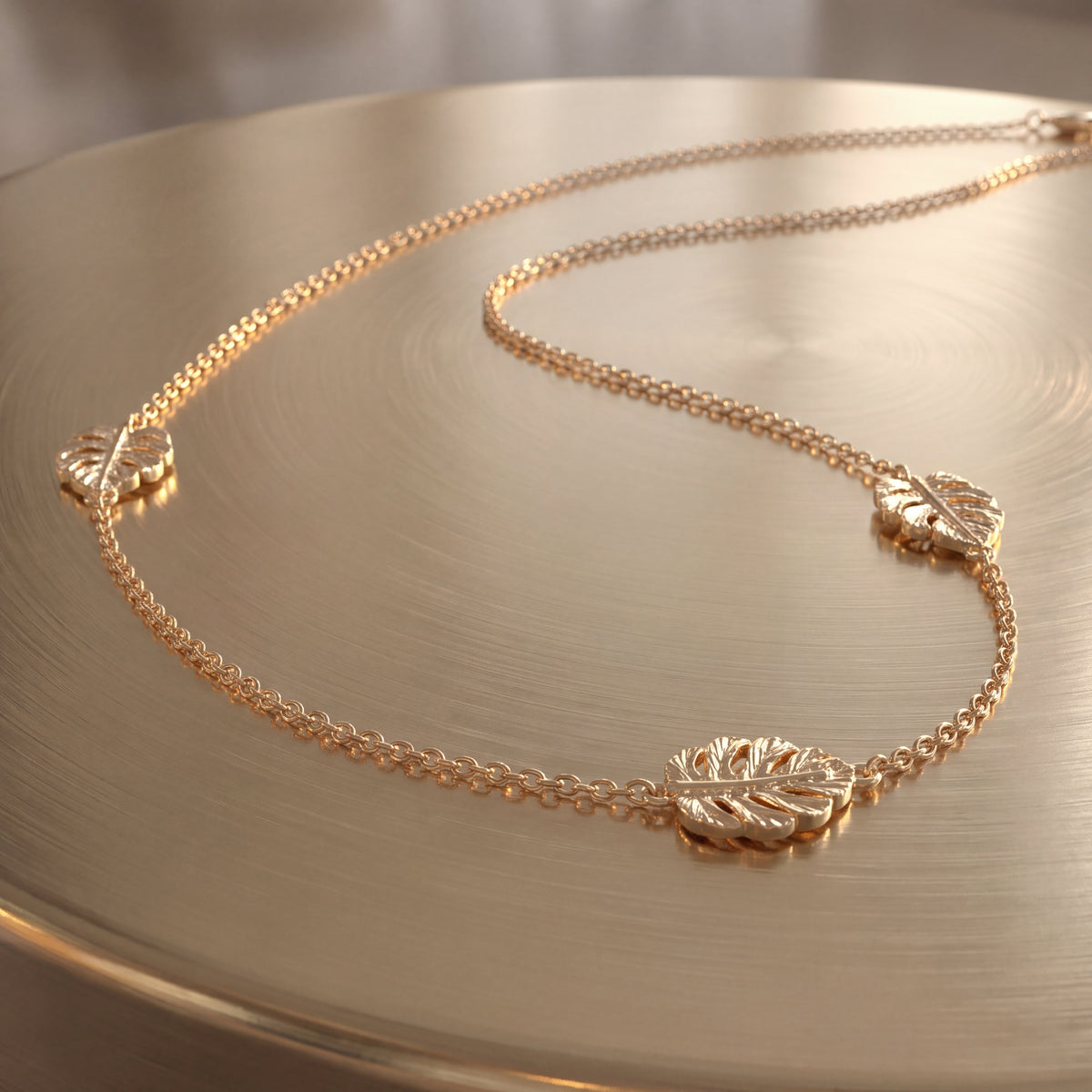 A gold chain necklace with openwork leaf stations spaced along it, on a warm gold surface.
