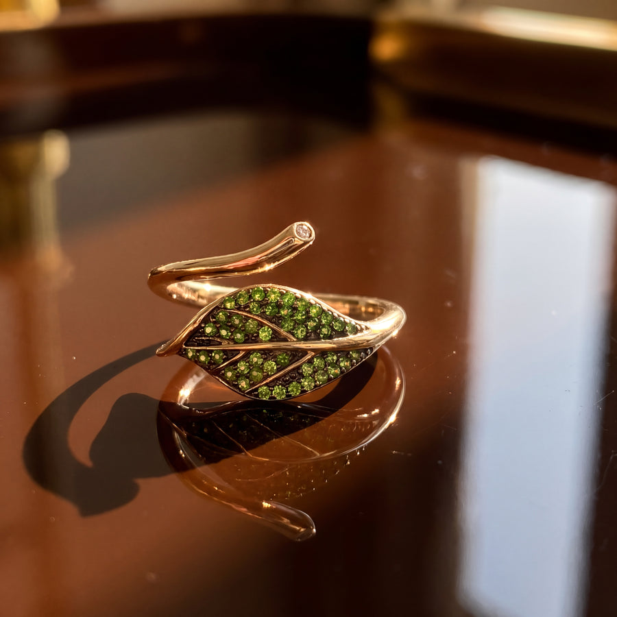 Yellow gold bypass ring with a leaf pave-set in green tsavorites and a curving stem