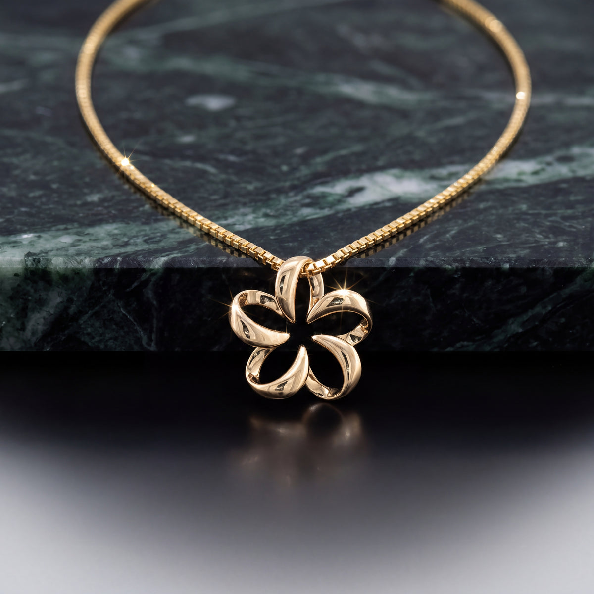 A yellow gold open-petal flower pendant on a fine chain, lying on dark green marble.