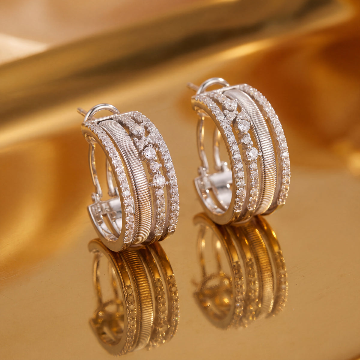 Layered white gold hoop earrings with textured bands and diamond rows