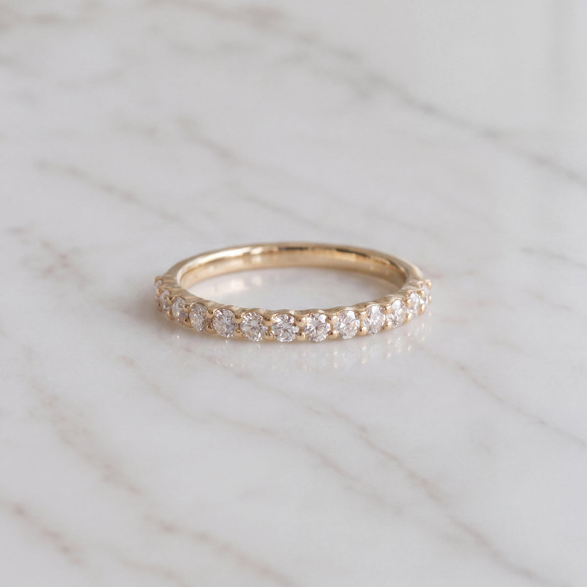 Slender yellow gold band of round diamonds in shared prongs