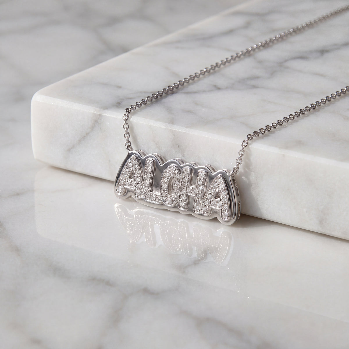 The word ALOHA in diamond-set white gold letters, lying on white marble.