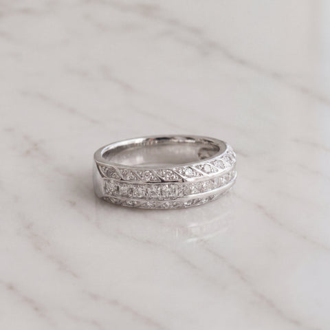 A white gold band of channel-set princess diamonds framed by milgrain and leaf-patterned metalwork.