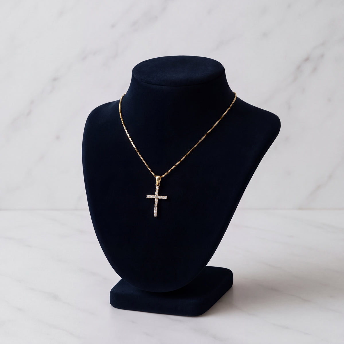 A slim gold cross pendant set with small diamonds, on a black velvet bust.
