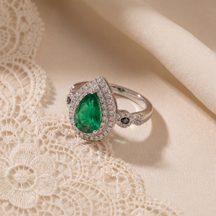 Pear-shaped emerald cocktail ring with a double diamond halo and twisted band in white gold