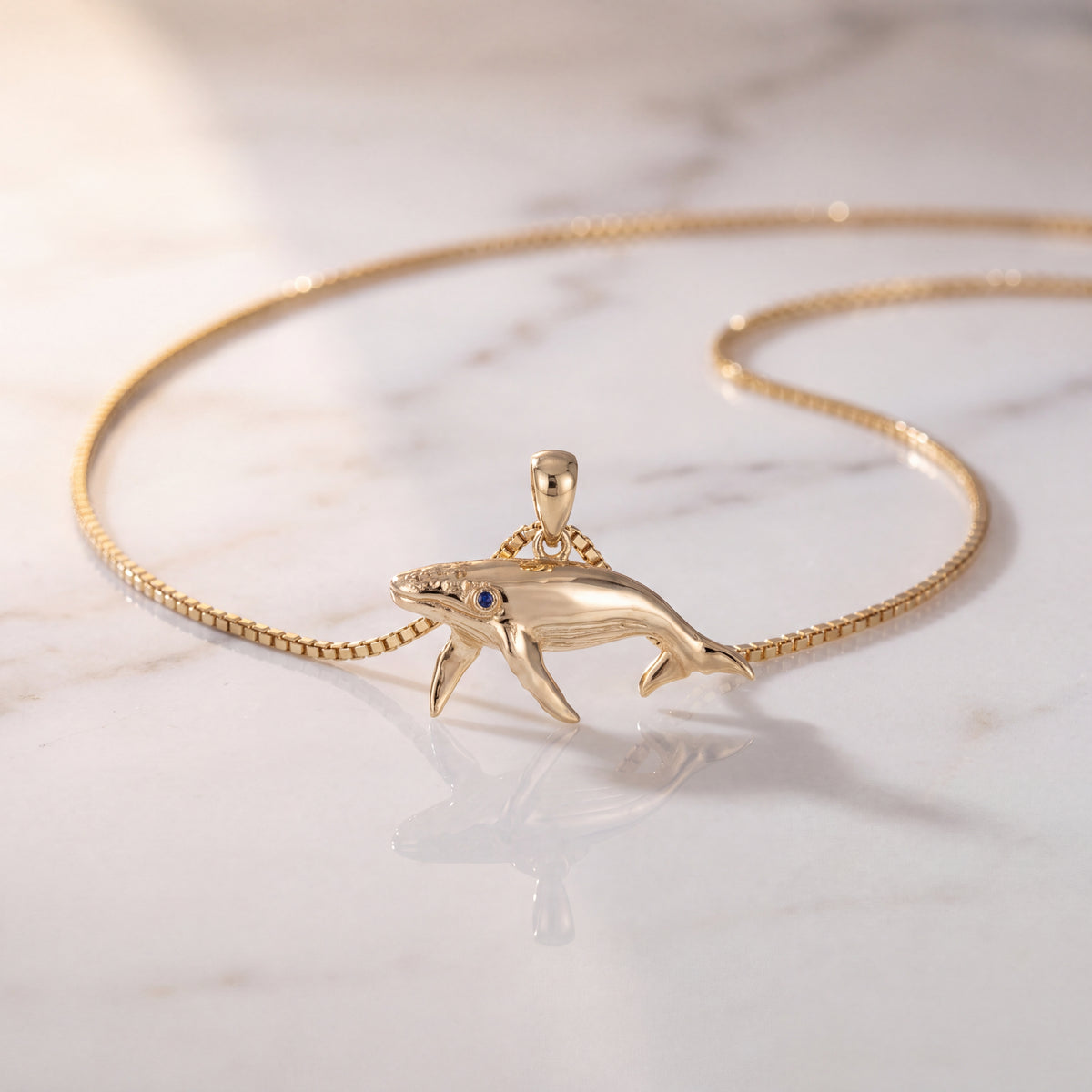 A gold whale charm on a fine chain, curved across a pale surface.
