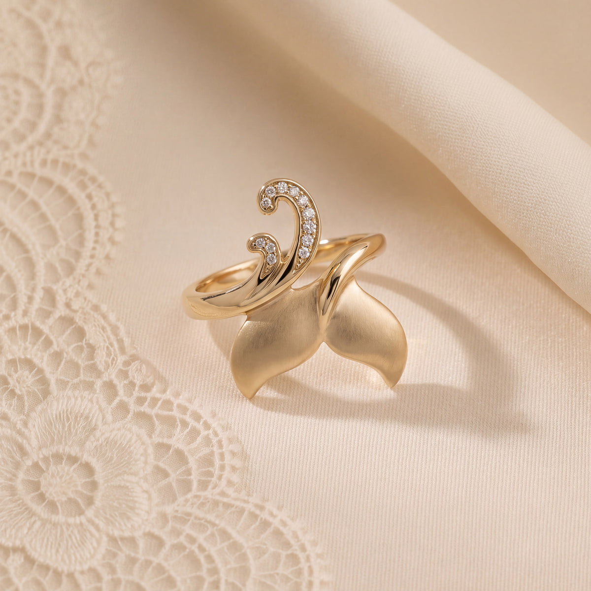 A whale tail cocktail ring with a diamond-set wave, resting on cream lace.