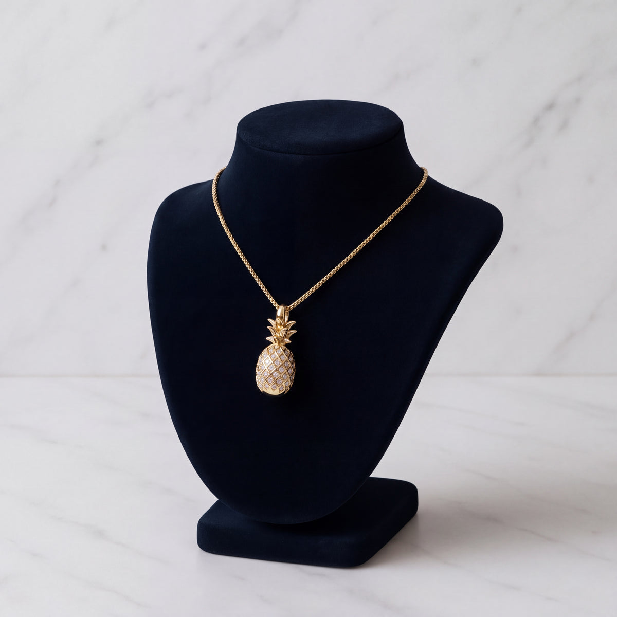 A gold pineapple charm with a diamond-set body, on a navy velvet bust.