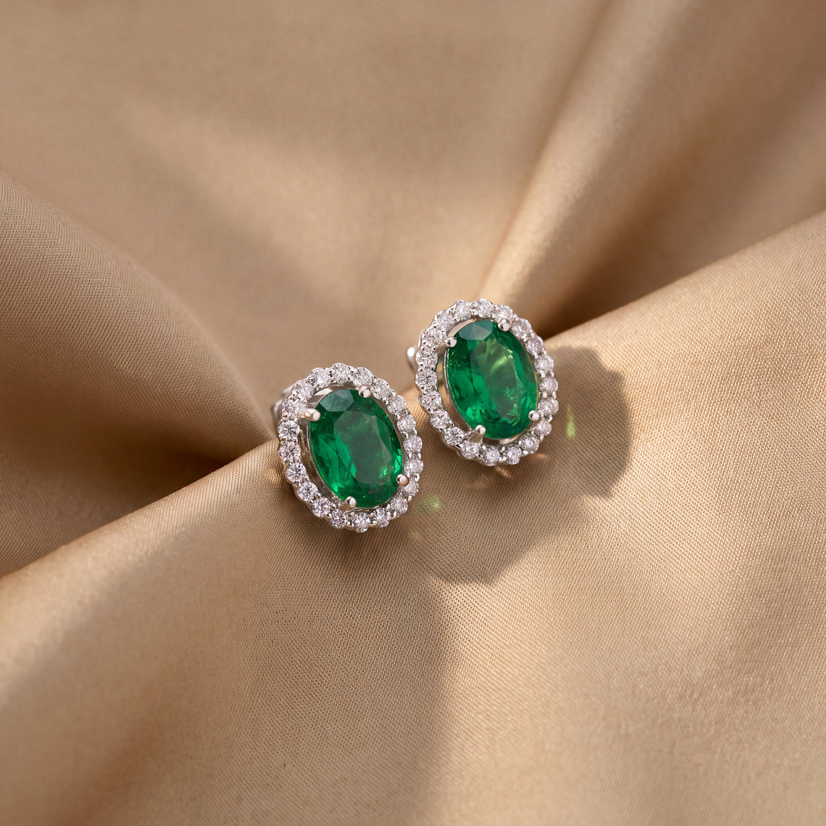 Oval emerald stud earrings with round diamond halos in white gold