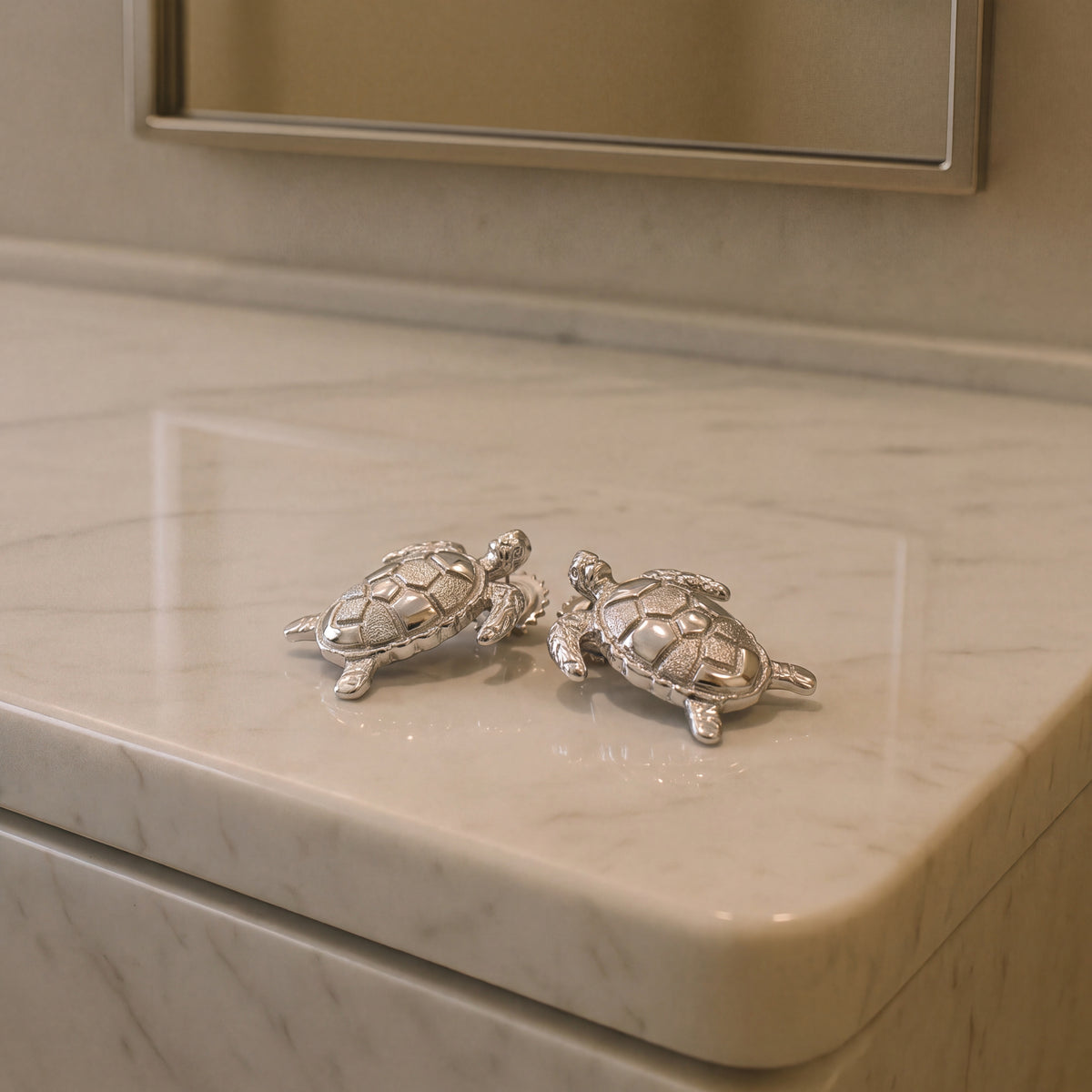 A pair of textured white gold sea turtle stud earrings on a marble counter.