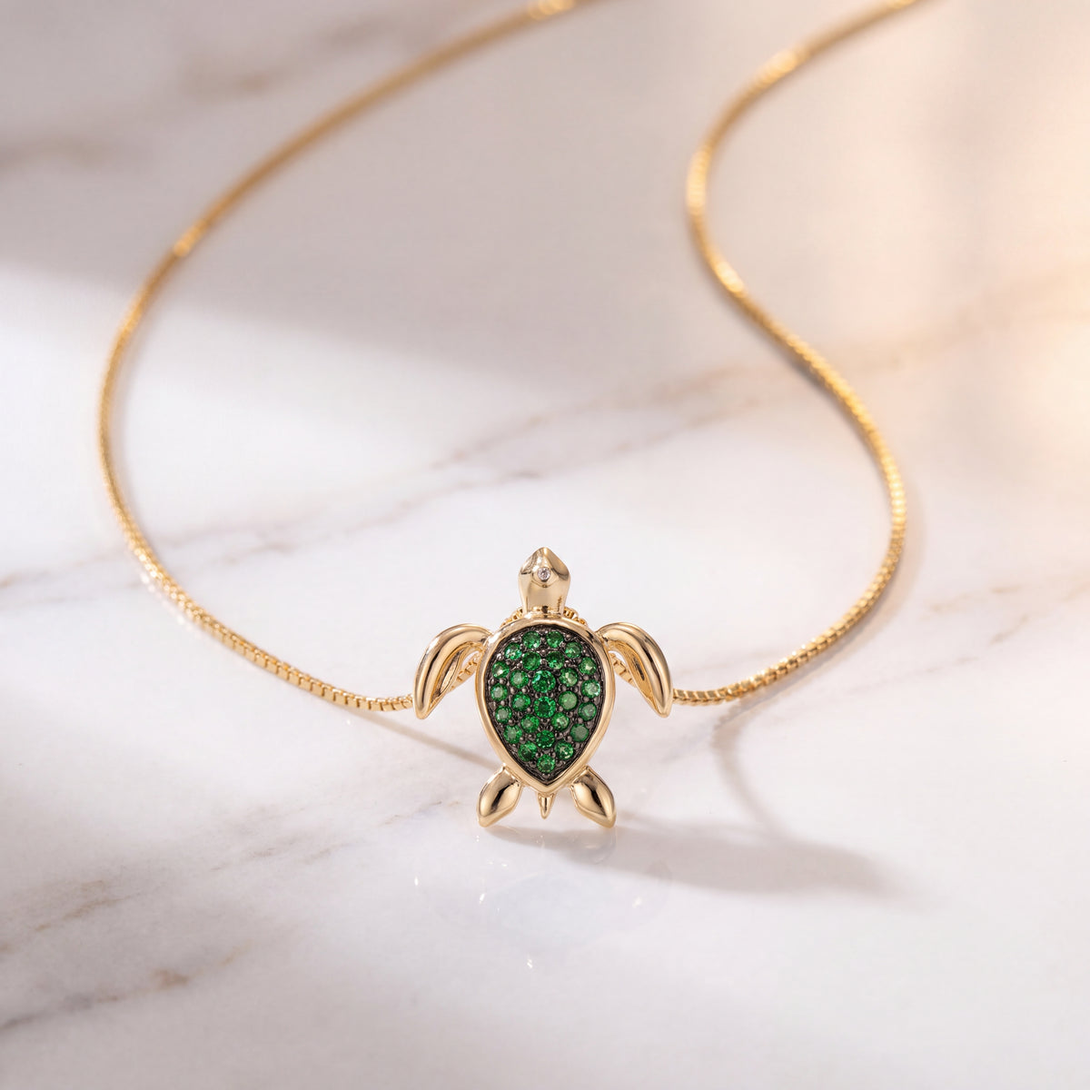 A gold sea turtle charm with a green-set shell, on a fine chain over a pale surface.