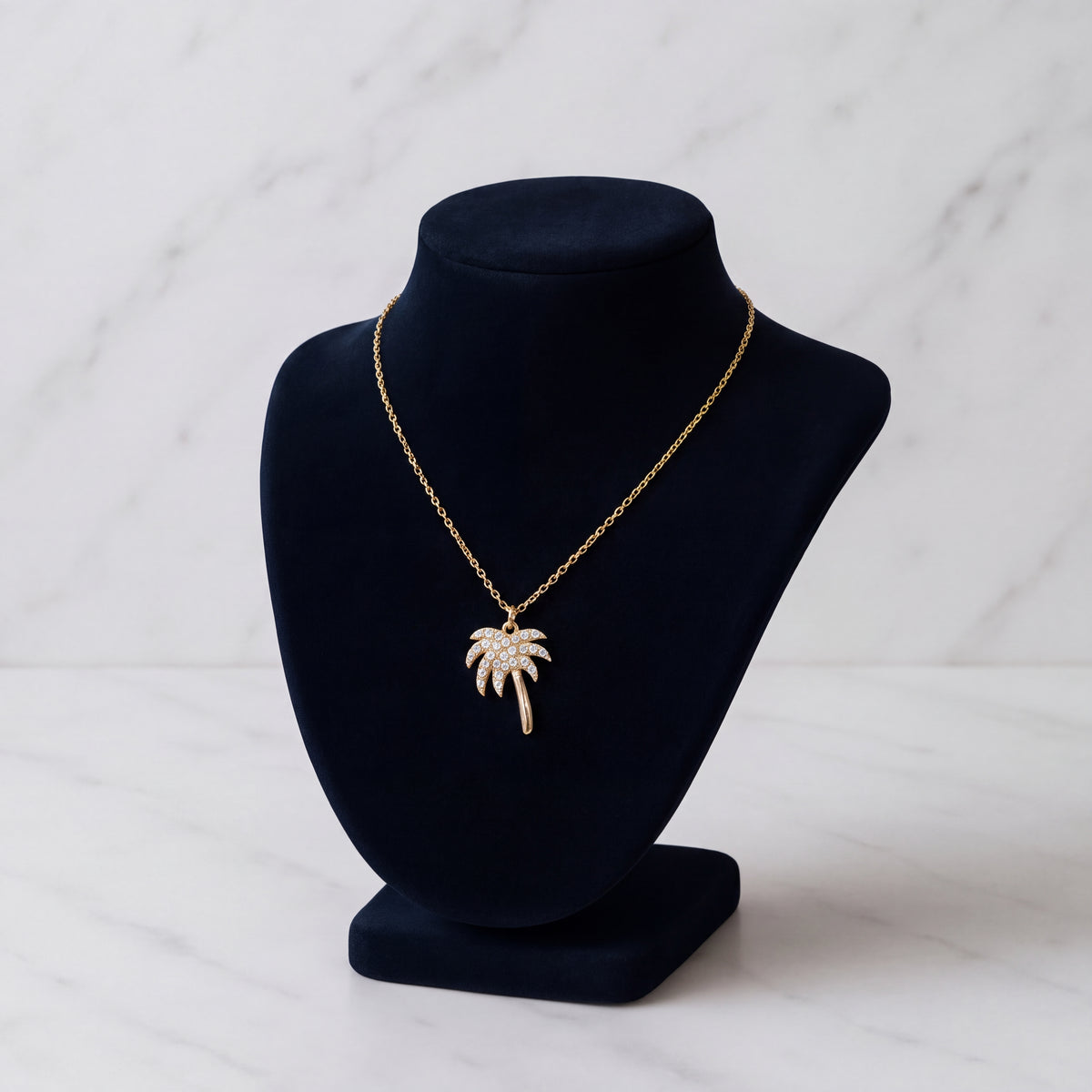 A yellow gold palm tree pendant with diamond-set fronds, hanging from a fine gold chain on a black velvet bust.