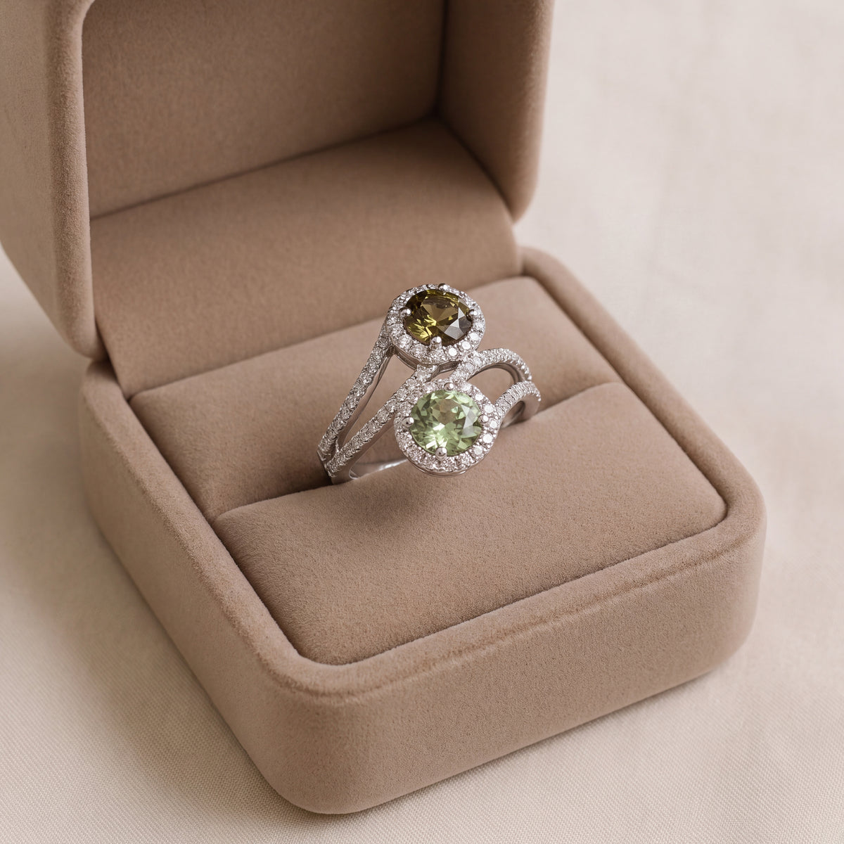 White gold bypass ring with an olive and a mint green round sapphire, each in a diamond halo on a pavé split shank