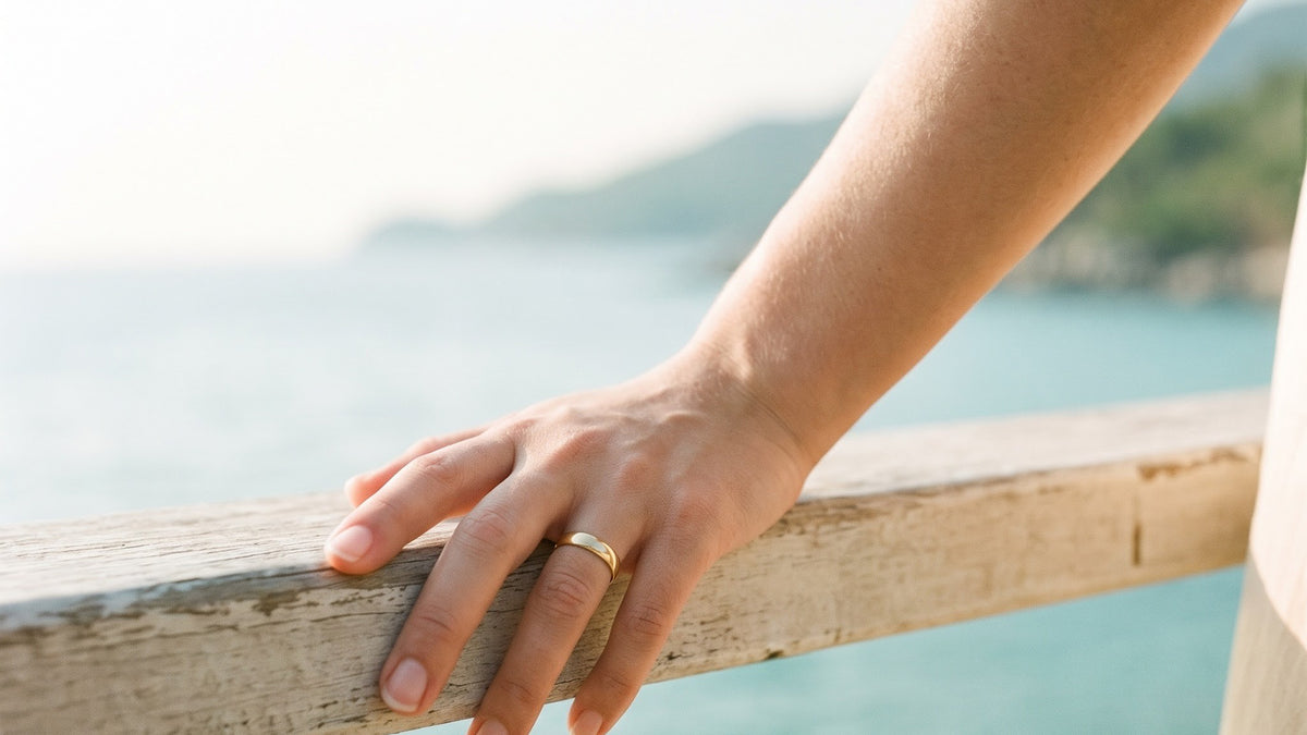 Hand with a thin band resting on a weathered wooden rail above a turquoise sea