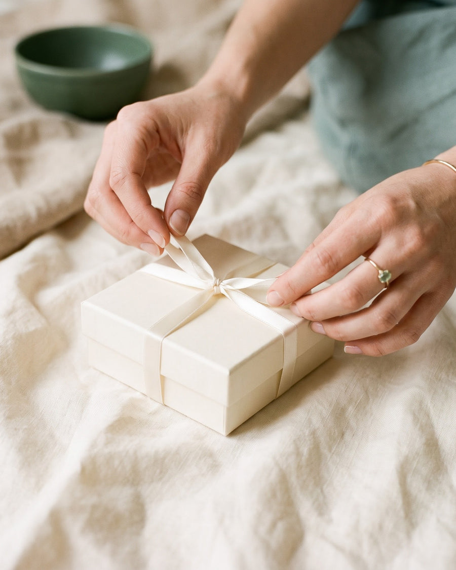 Hands untying an ivory ribbon on a small cream gift box