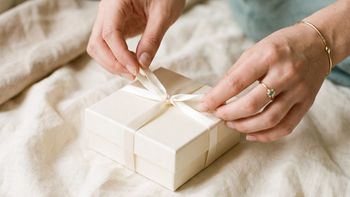 Hands untying an ivory ribbon on a small cream gift box