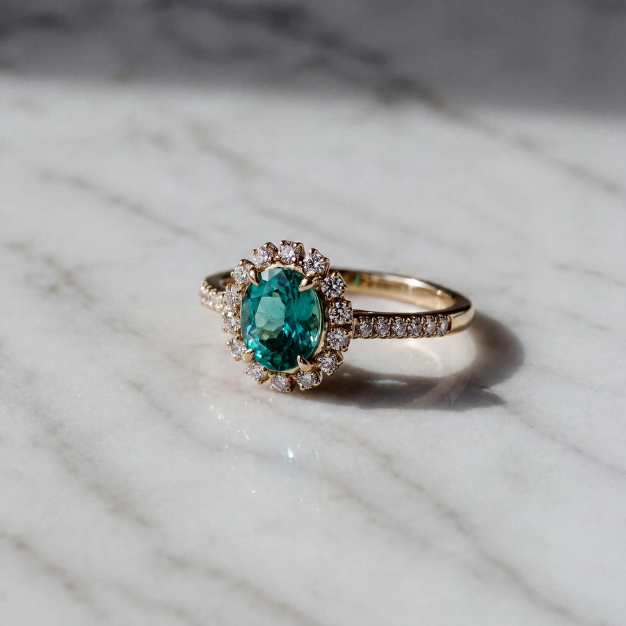 A blue-green oval stone in a diamond halo, on a yellow gold band