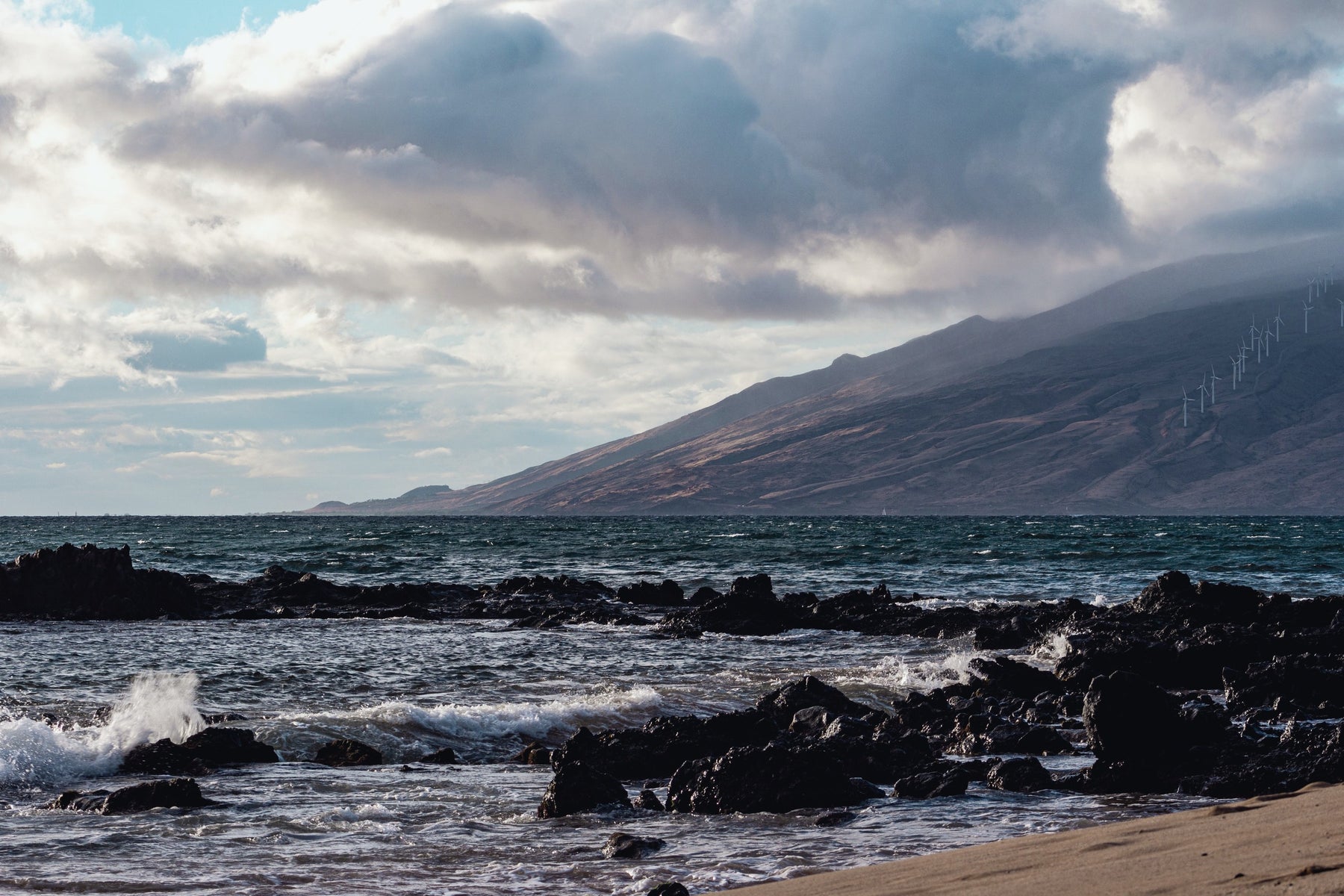Surf over lava rock with a mountain ridge beyond