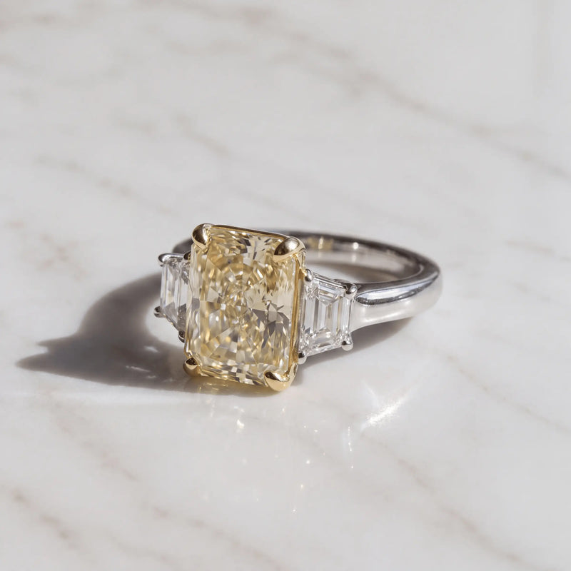 A yellow radiant-cut three-stone ring on pale marble