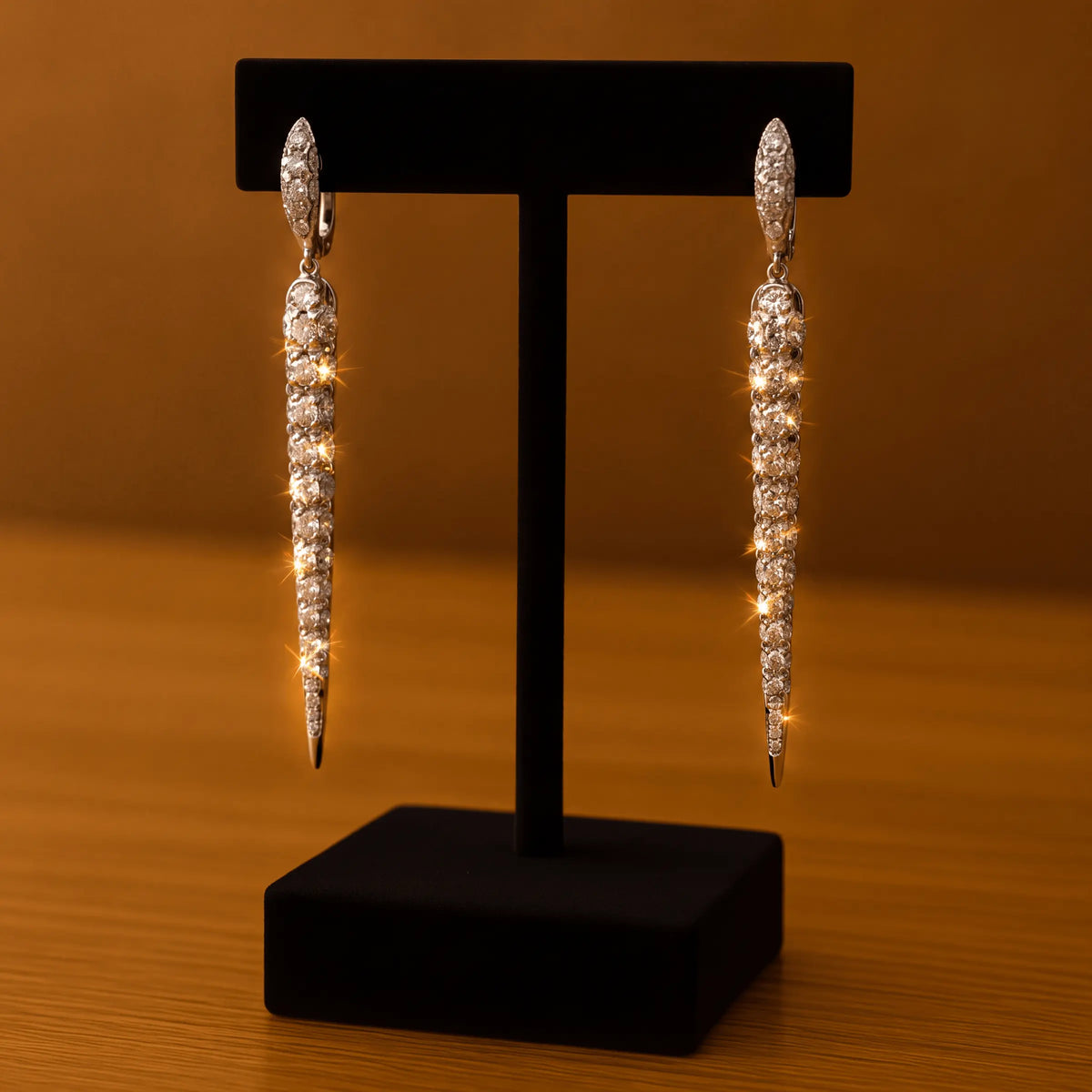 A pair of diamond drop earrings on a stand, warm amber light