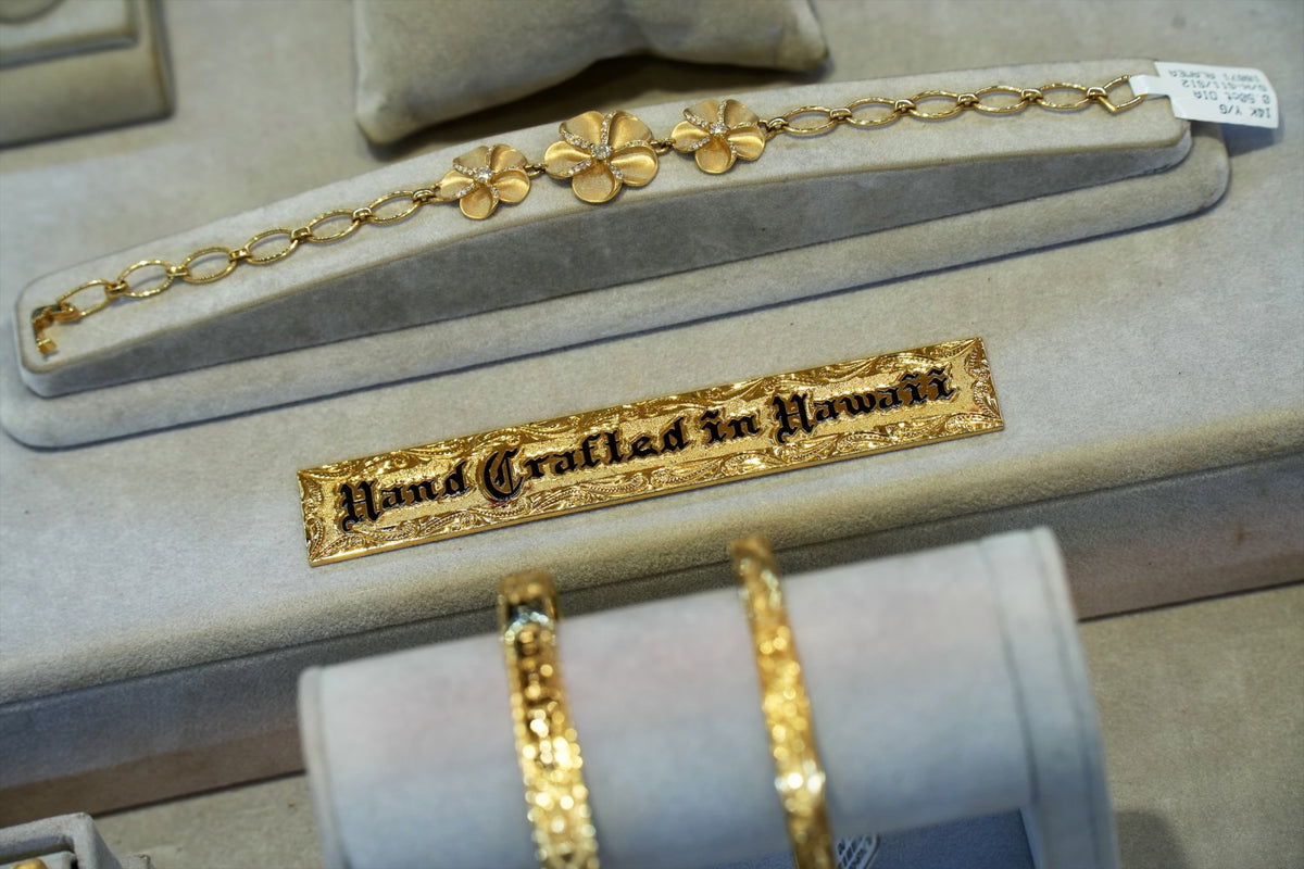 A gold plumeria bracelet and gold bangles beside a Hand Crafted in Hawaii plaque