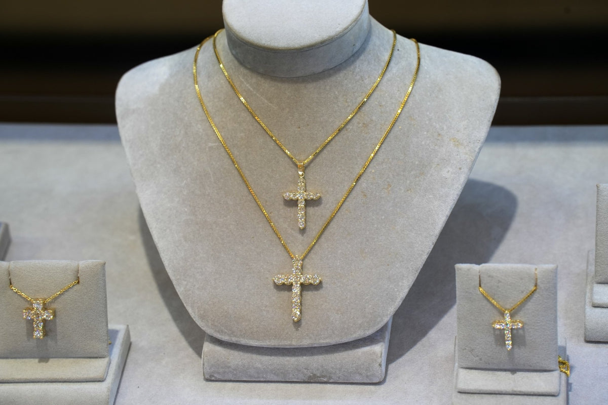 Two gold diamond cross necklaces on a display bust in the case