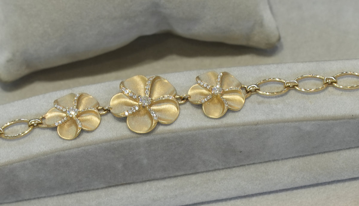 A diamond plumeria bracelet in yellow gold in the case at Greenleaf Diamonds