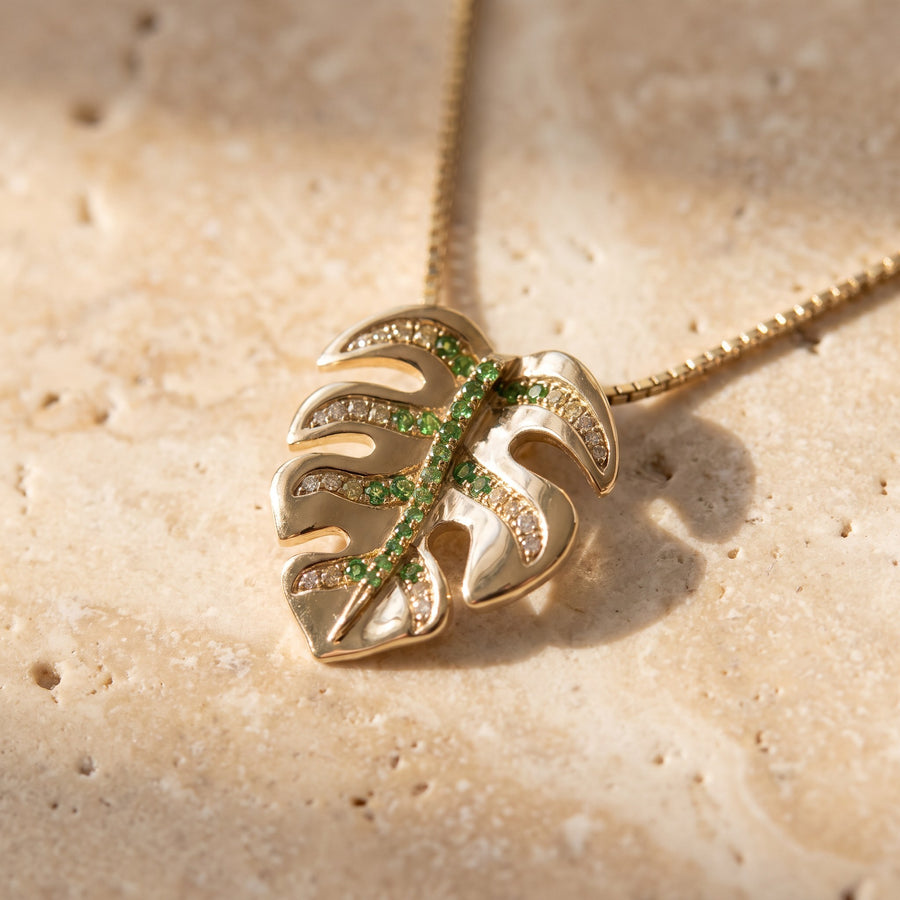 Yellow gold monstera leaf pendant with green stones along the vein