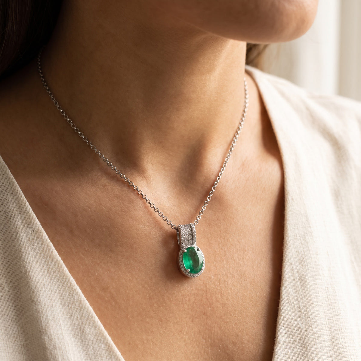 Oval Emerald and Diamond Halo Pendant in White Gold, worn