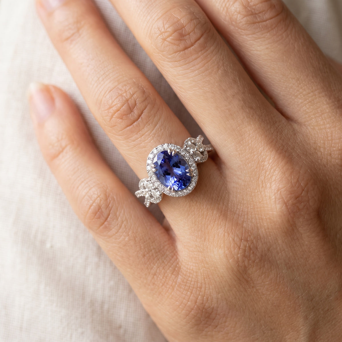 Oval tanzanite white gold ring with a diamond halo and diamond knot shoulders, worn