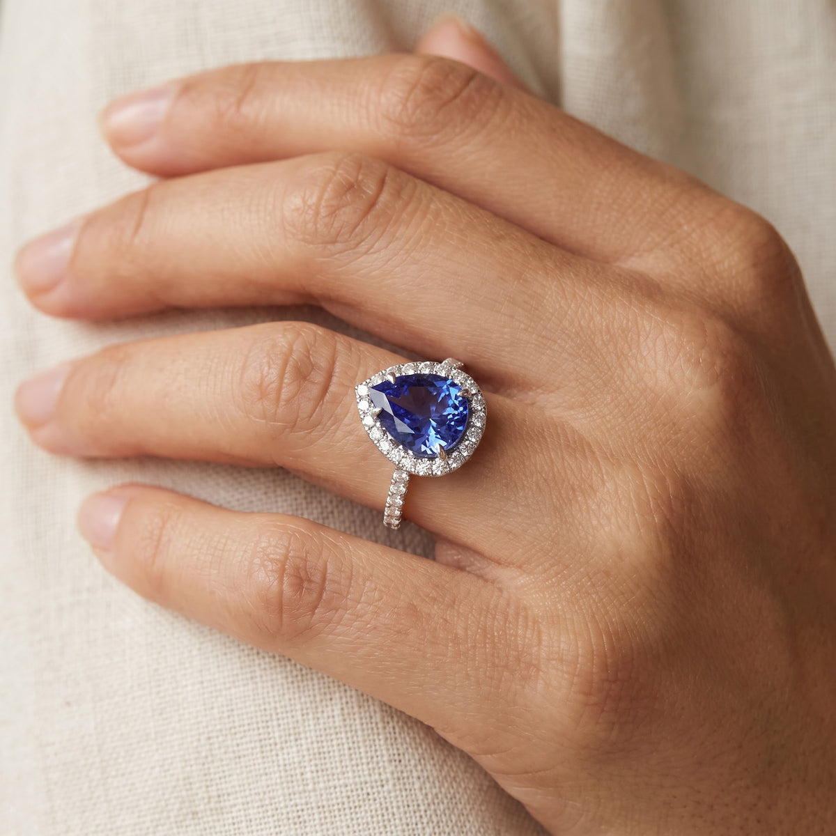 Pear-shaped tanzanite in a diamond halo on a slender white gold band, worn