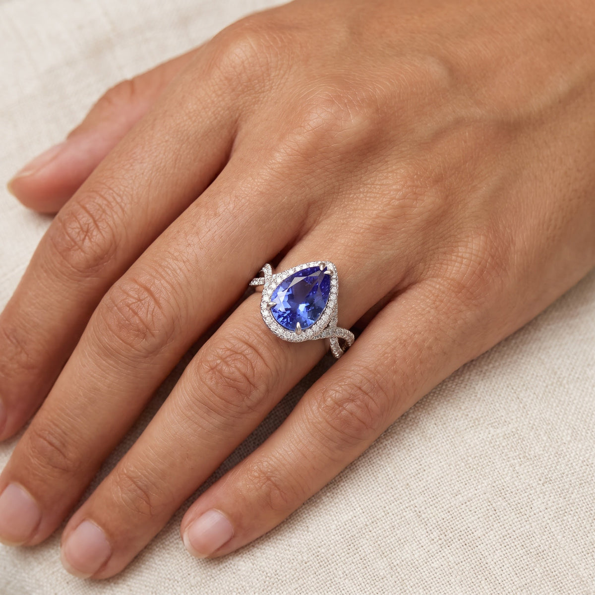Pear-shaped tanzanite ring with a diamond halo on a twisted white gold split shank, worn