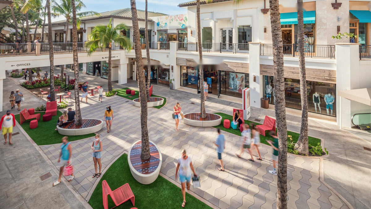 The courtyard at the Shops at Wailea by day: palm trees, red chairs and lawn between the shops