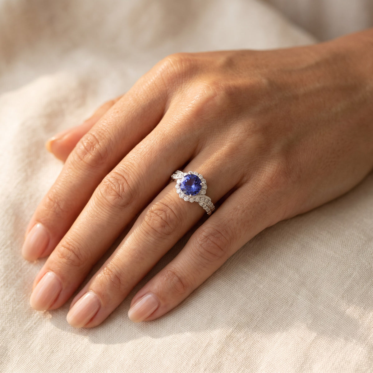 Round tanzanite white gold ring with a diamond halo and twisting diamond-set shoulders, worn
