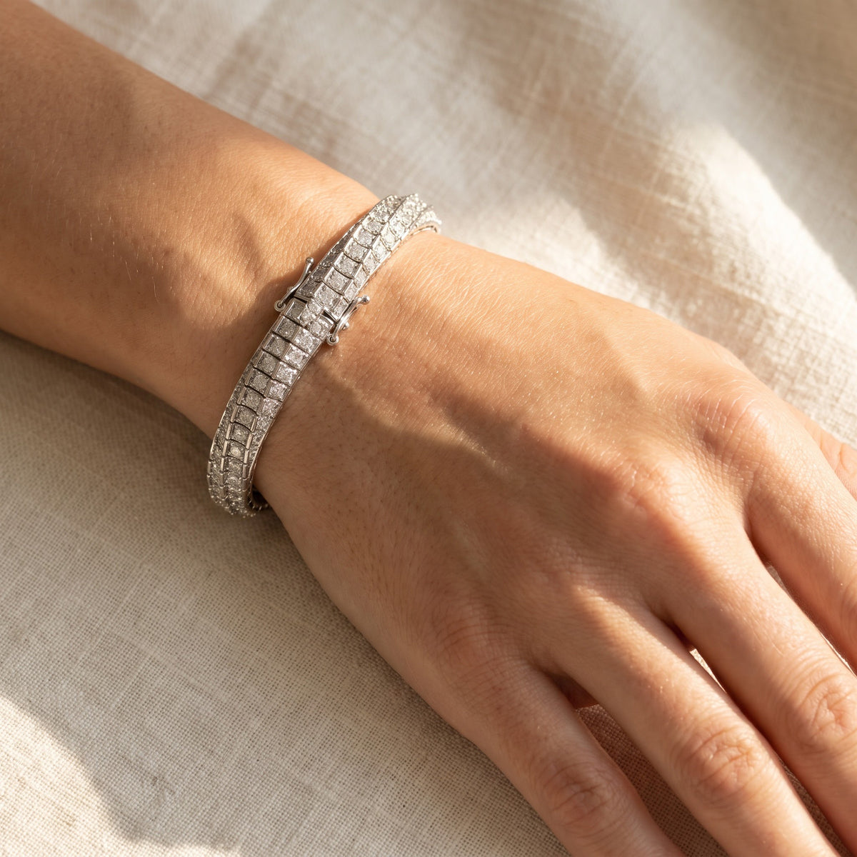 Wide white gold bracelet set with rows of round diamonds and a box clasp, worn