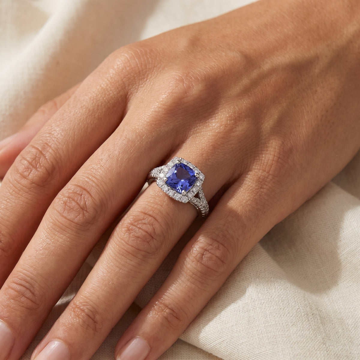 Cushion tanzanite in a diamond halo on a pavé white gold split shank, worn
